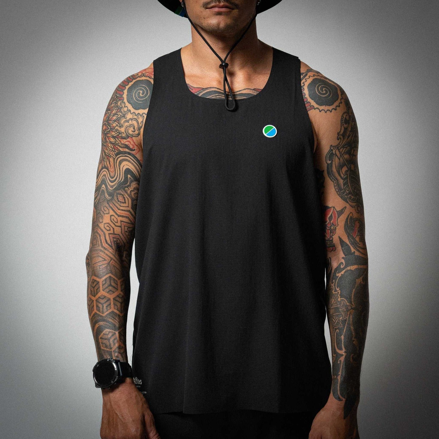 Aeria Fortis Race Tank in black worn by a model, showcasing breathable recycled ripstop fabric with silicone chest patch for runners.